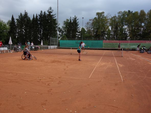 Tennisplatz mit zwei Spielerinnen, eine Spielerin Sitzt im Rollstuhl